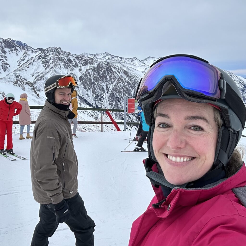 A woman and a man in ski attire smile at the camera on the piste