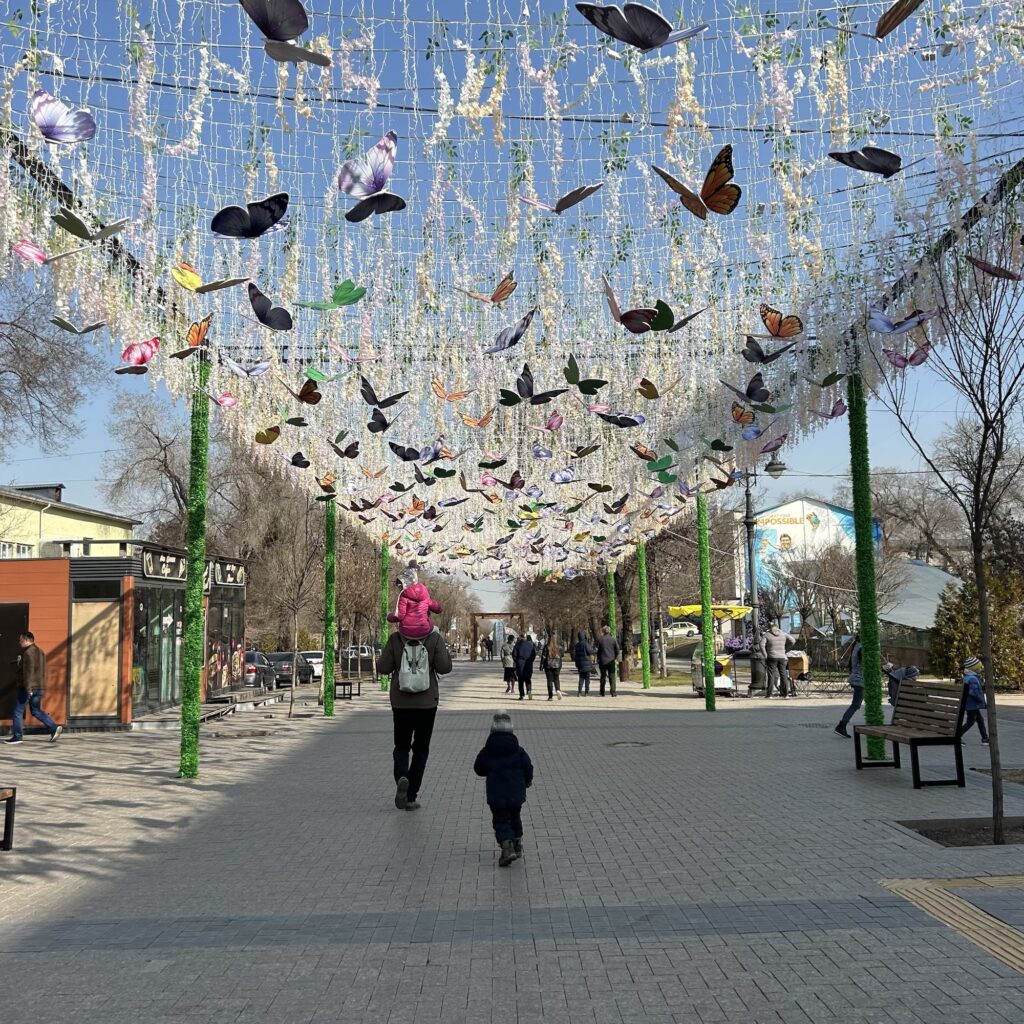 A man and his children walk into the distance along a street with spring decorations above their heads