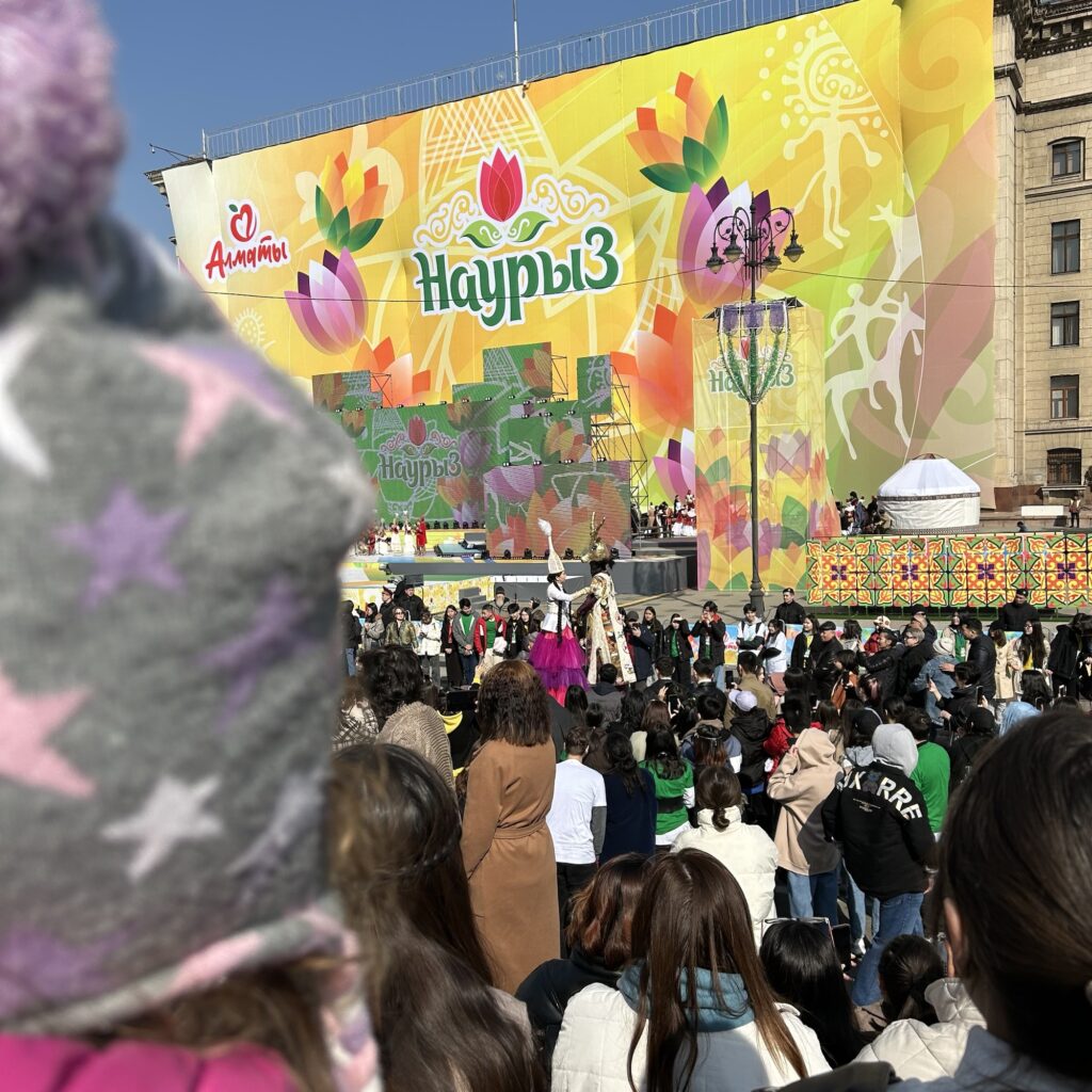 Astana Square is decorated with a brightly coloured banner celebrating Nauryz, in the foreground is a child's head covered by a winter hat