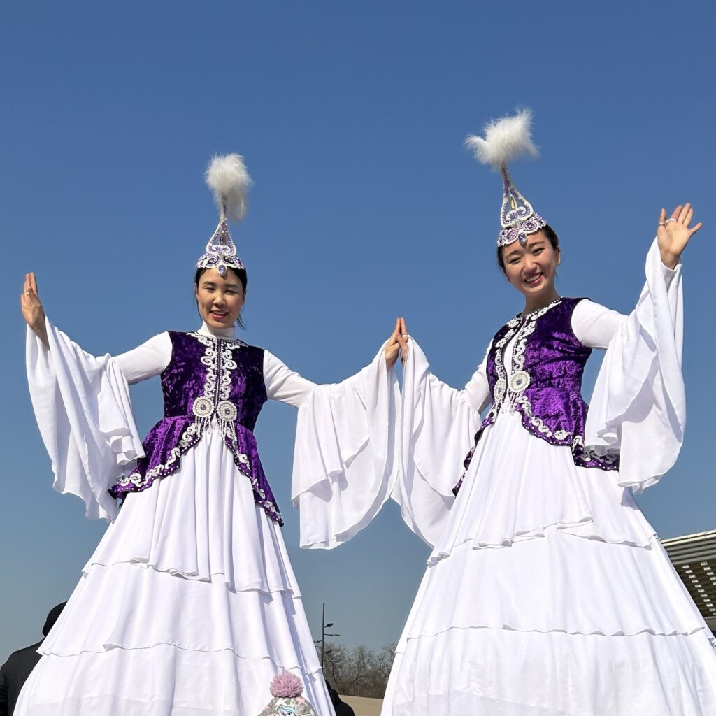 Two young female performers in Kazakh tradition outfits pose for a photo on Nauryz