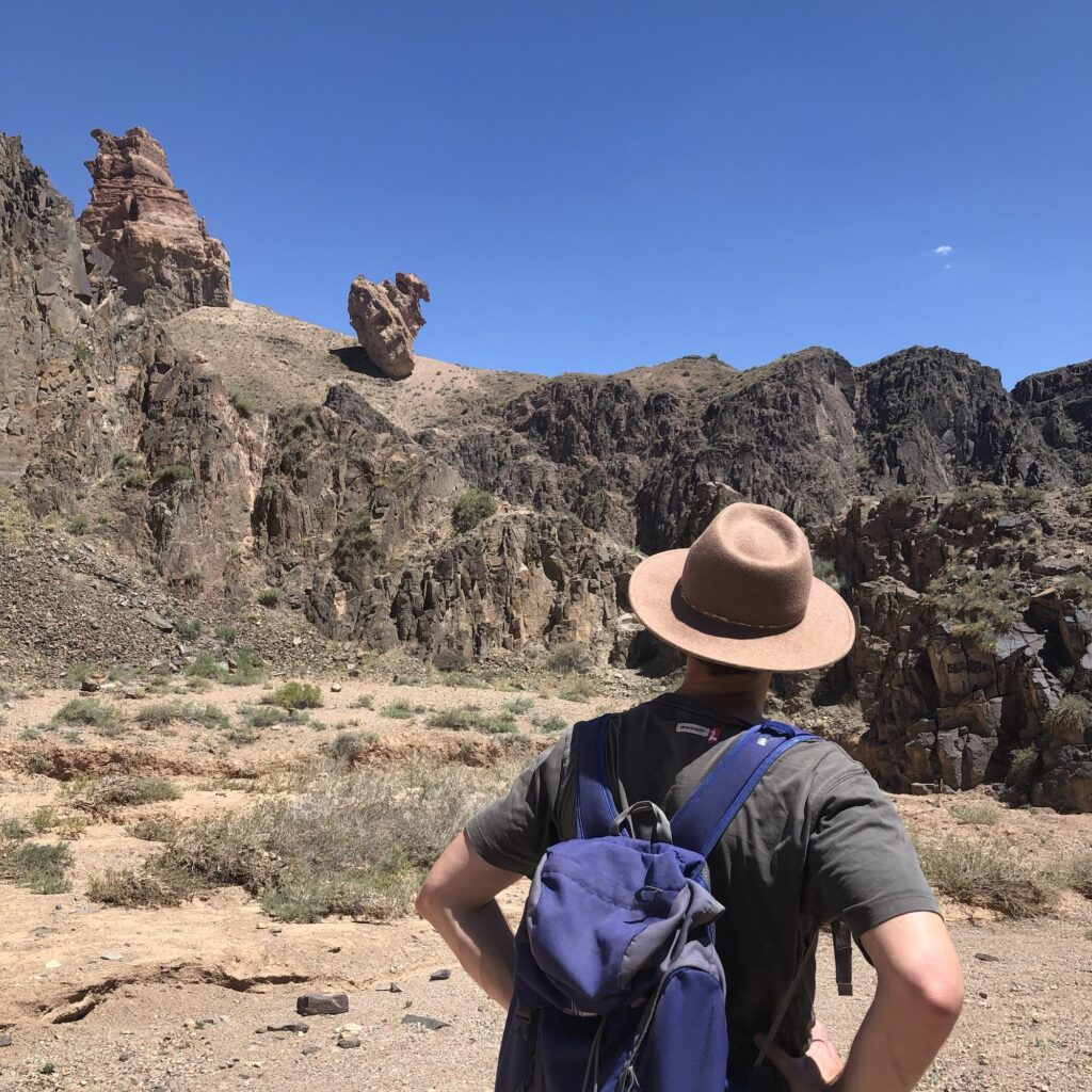 a man stops mid hike to look up at interesting geological formations in Charyn Canyon, Kazakhstan