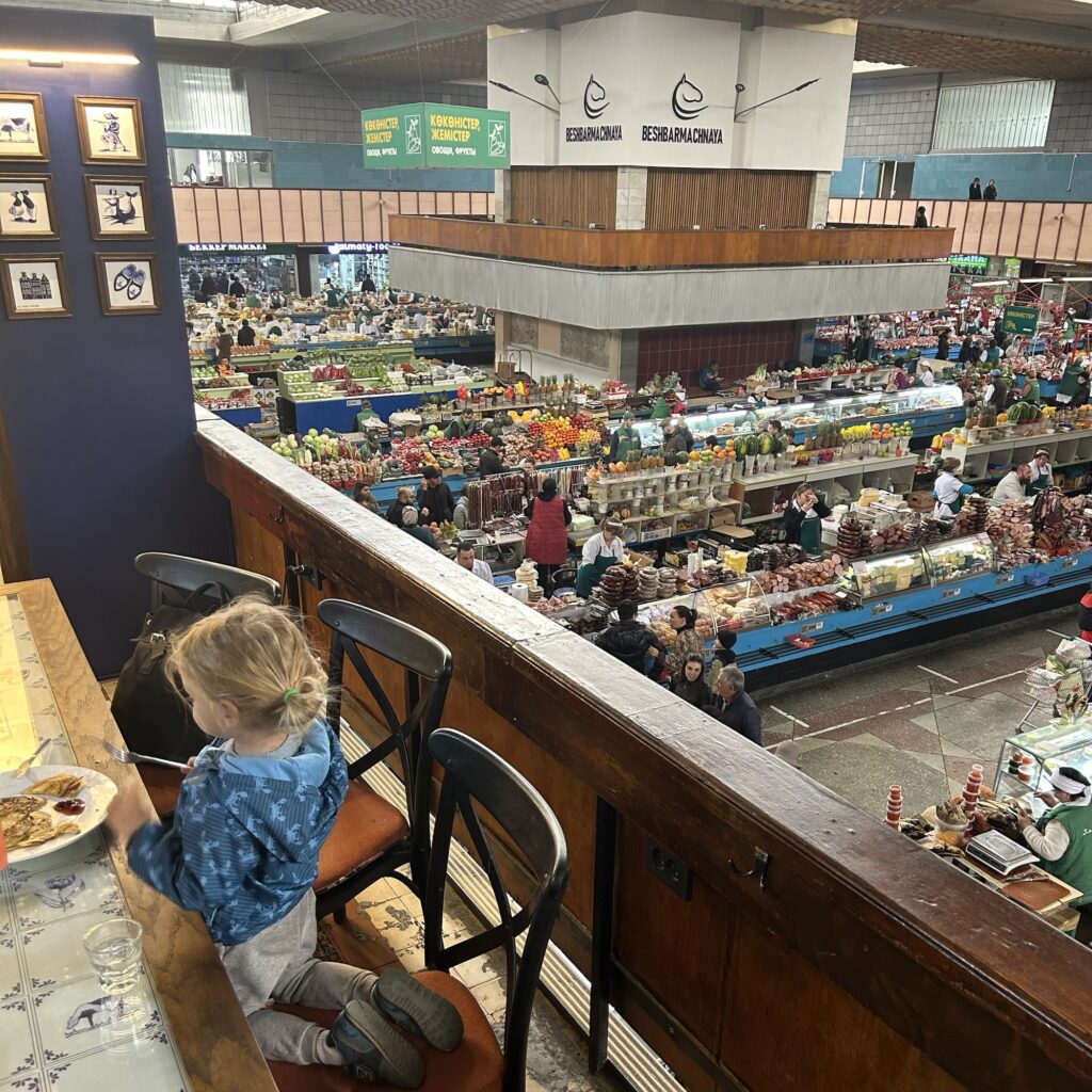 a small child sits at a cafe table on a balcony above the bustling Green Bazaar in Almaty