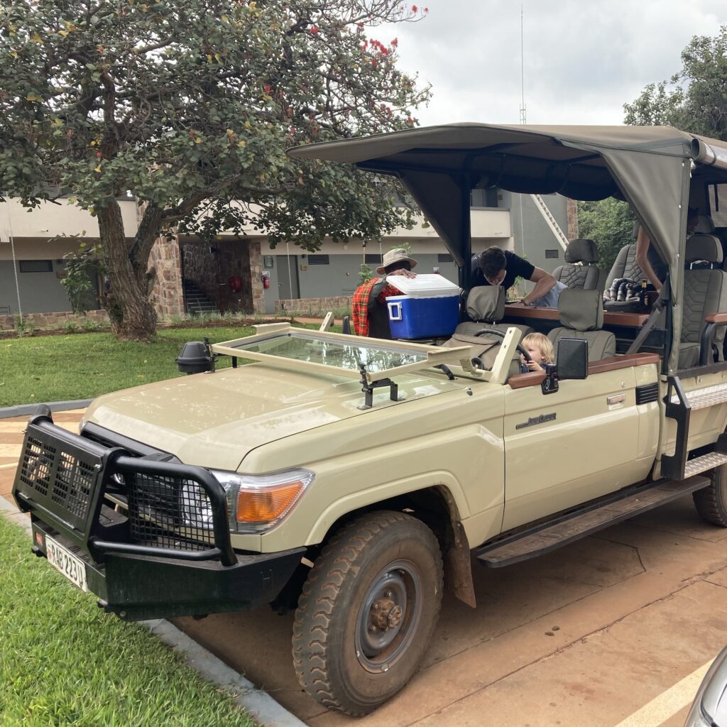 A little boy sits in the driver's seat of a big khaki safari jeep at Akagera while the jeep is loaded with supplies