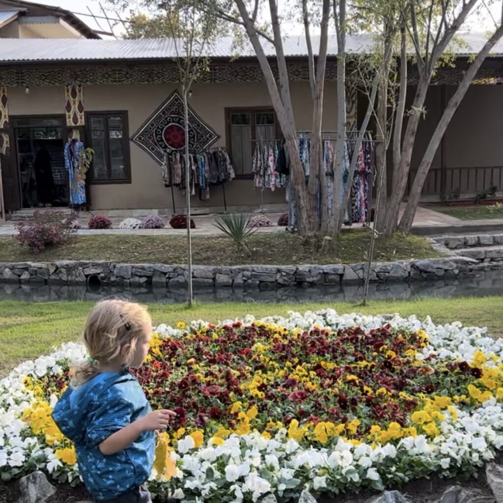 A small boy runs in front of a flower bed in Konigil, the paper making village in Samarkand, Uzbekistan