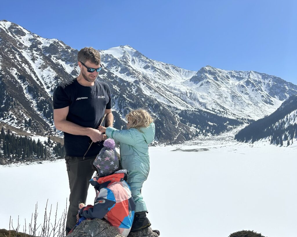 A man stands with his children in front of the stunning frozen Big Almaty Lake