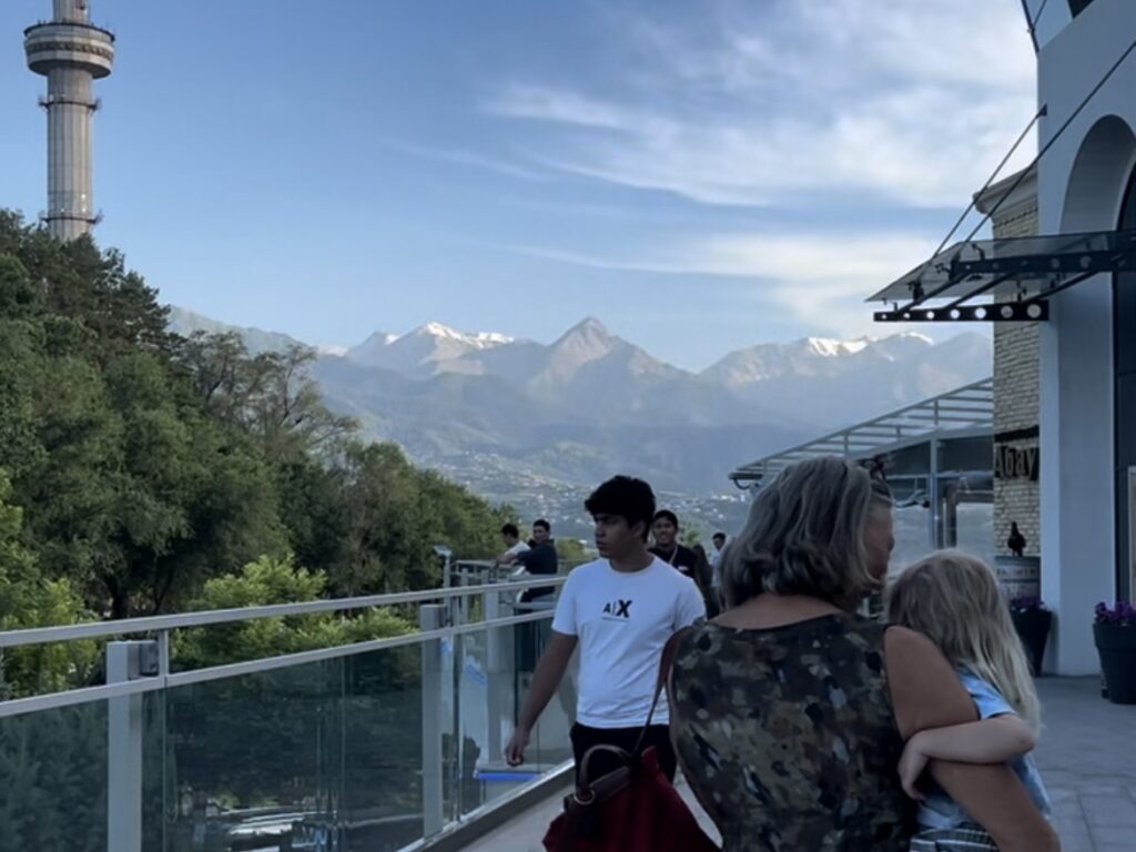 a woman carries a child while walking towards a restaurant with mountains in the background