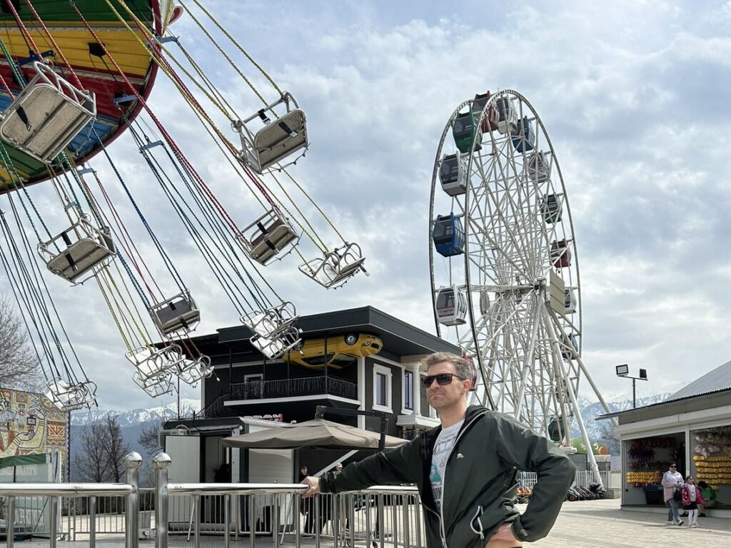 a man watches the c hair swing ride at Kok Tobe, with the upside down house and the ferris wheel in the background