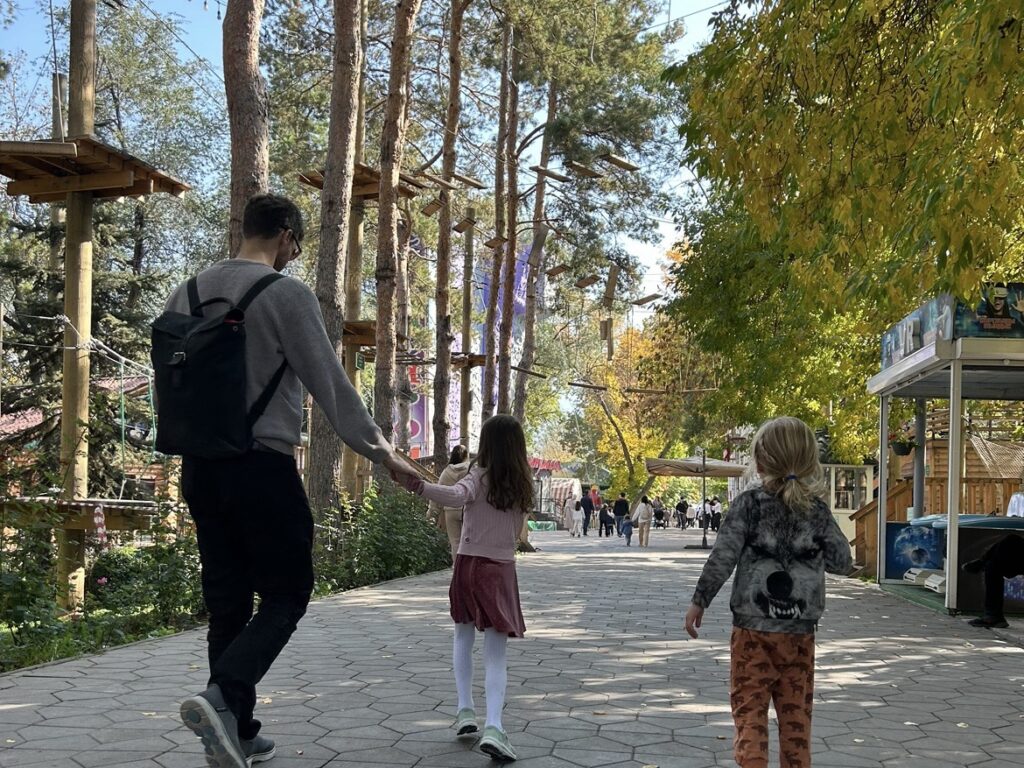 Two small children lead their father through a forested fairground