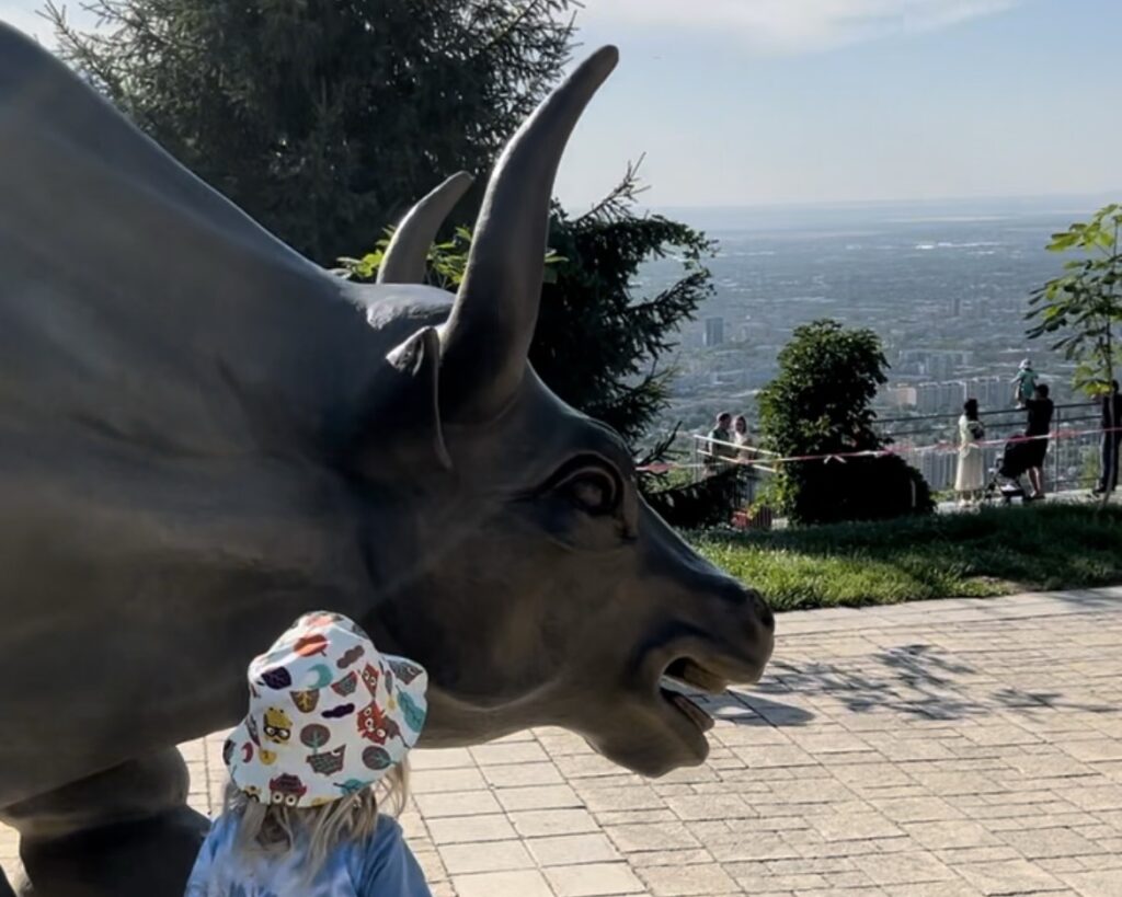 A small child looks at a replica bull statue from the famous one at Wall St, on Kok Tobe overlooking Almaty 