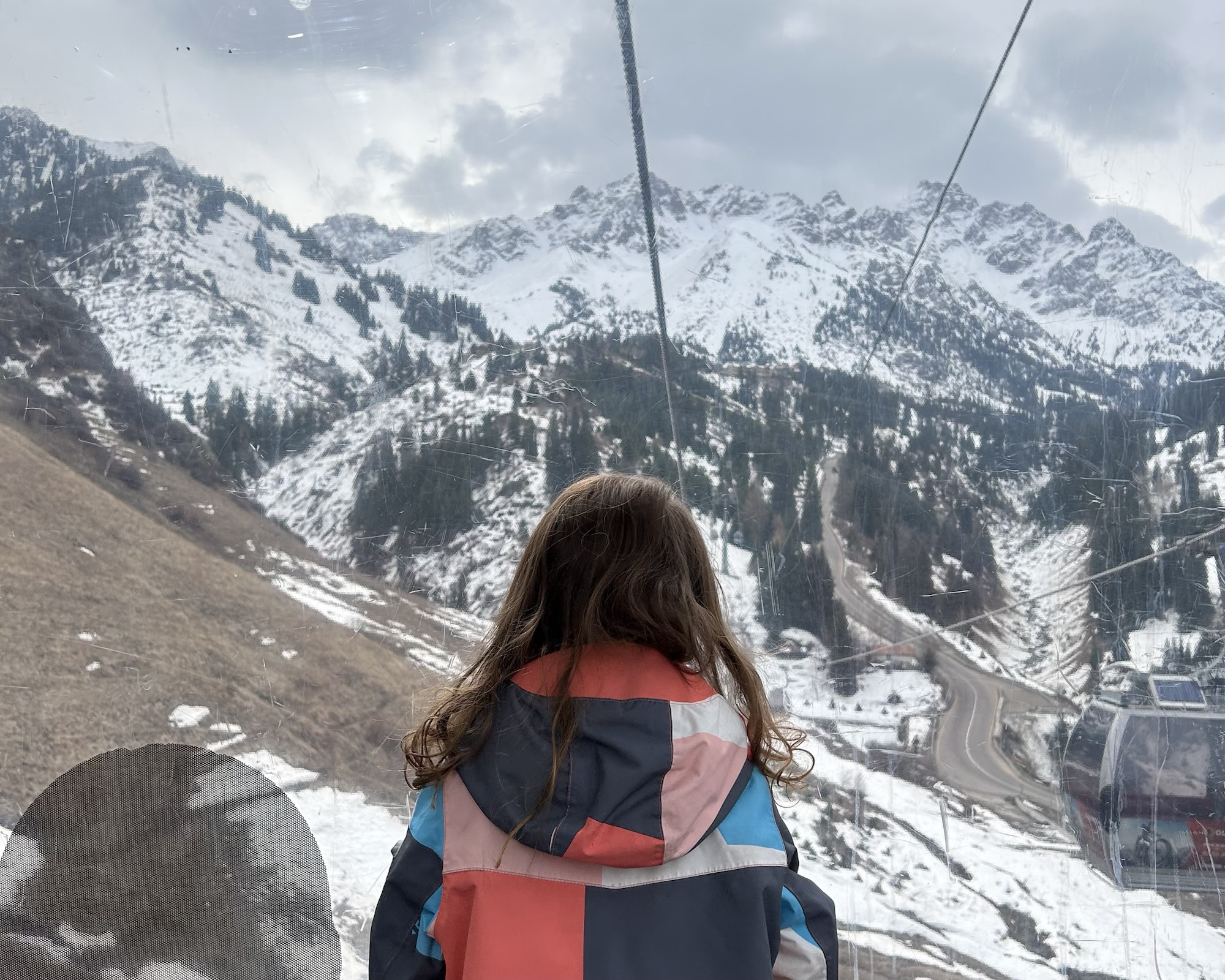 A girl looks out the window of a gondola cabin towards the snowy mountains she is travelling towards