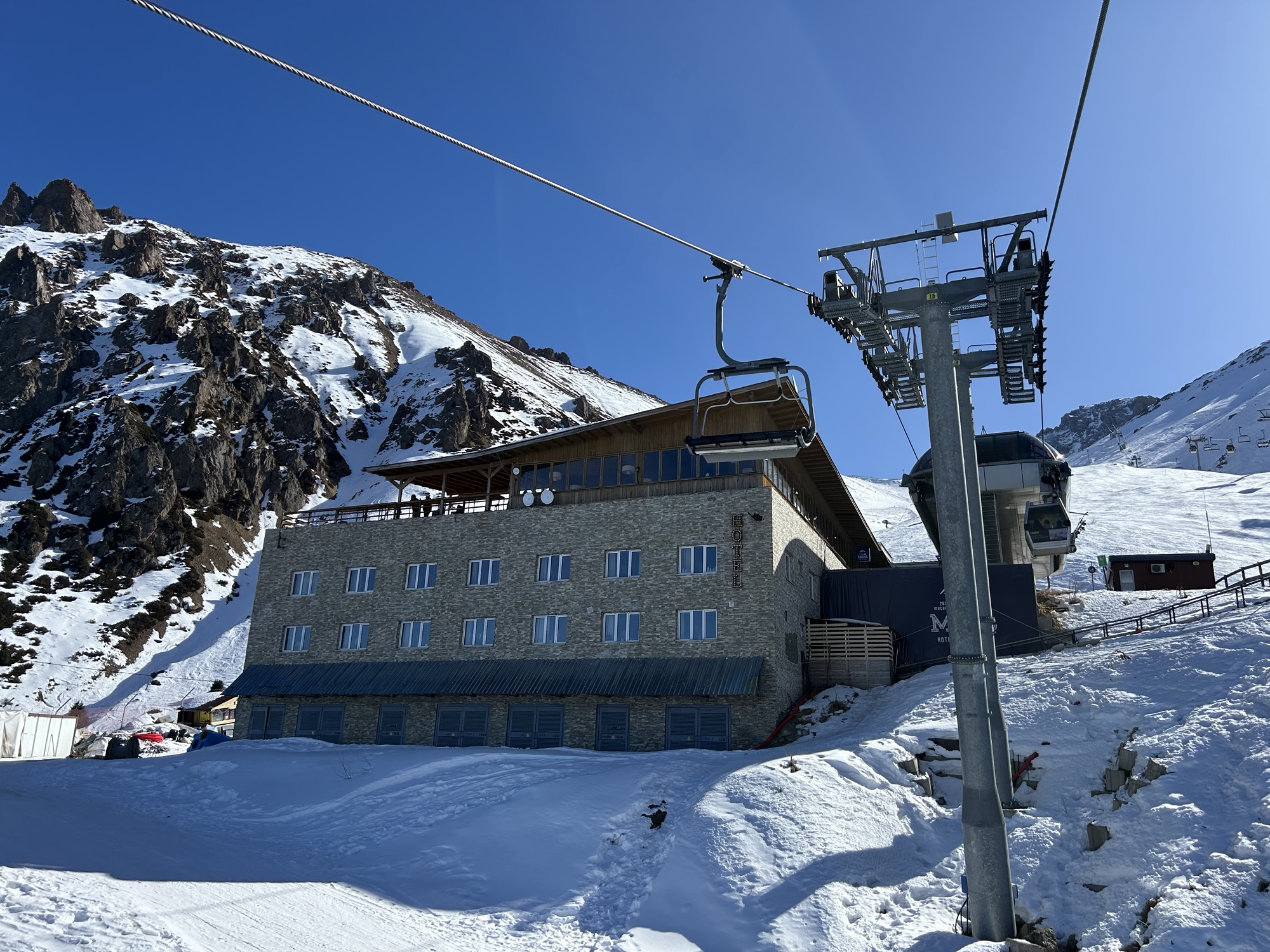 An imposing concrete building situated next to a chairlift stands in the foreground with a snowy mountain behind.