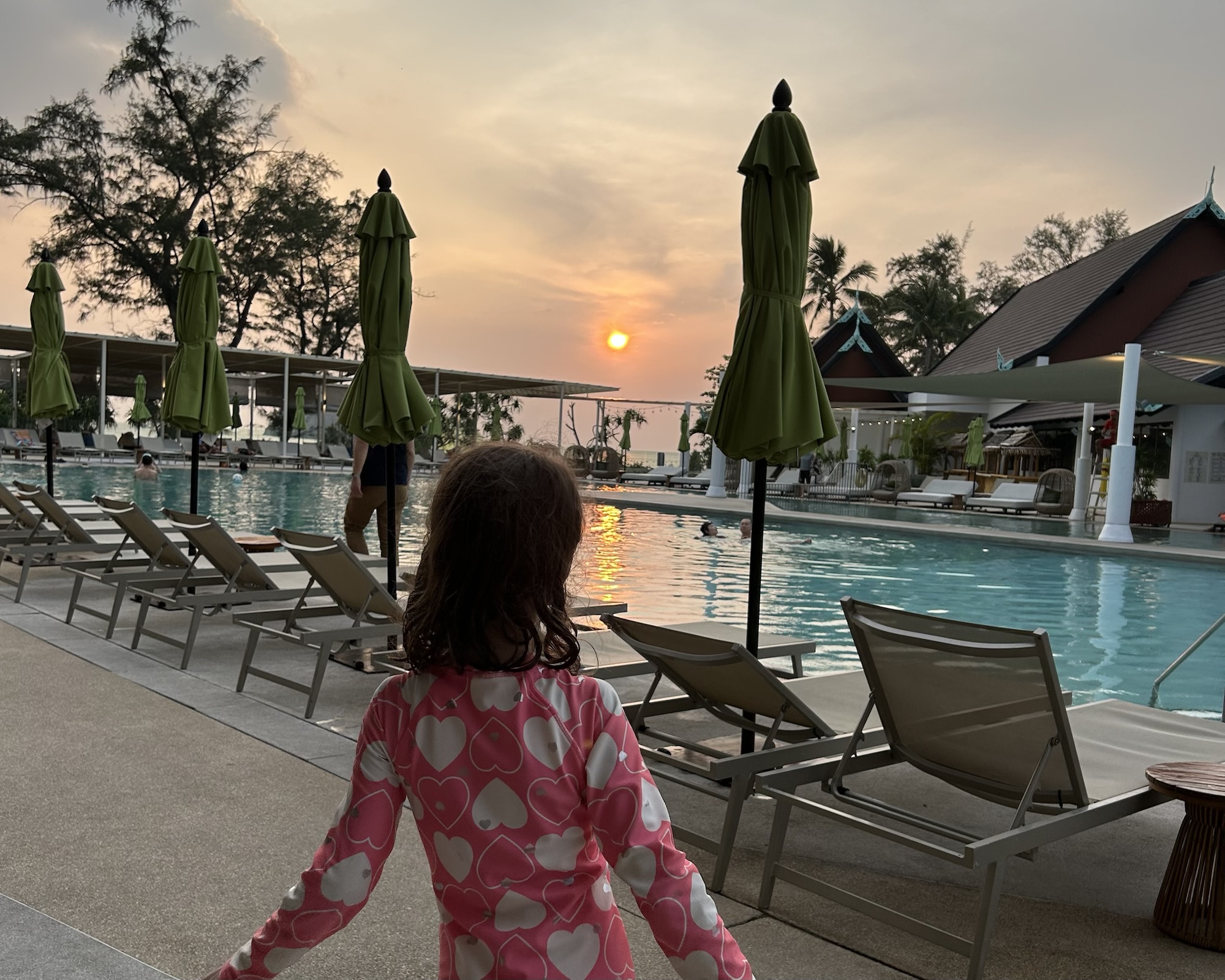 A photo of a small girl facing the pool at Club Med Phuket with the setting son in the background