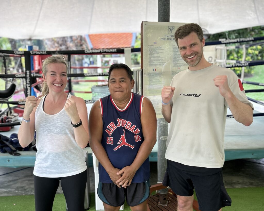 A Photo of a woman and two men in training outfits in front of a boxing ring