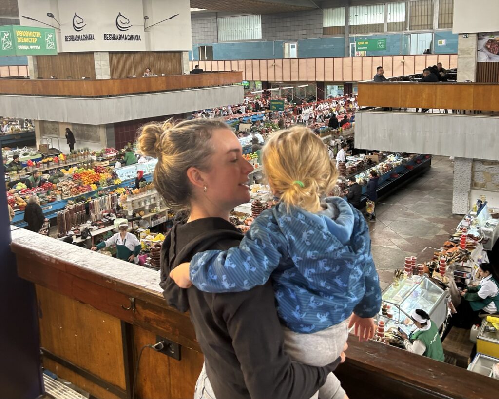 A photo of a woman holding a child looking down over Almaty's Green Bazaar from the balcony of Bowler Coffee Shop