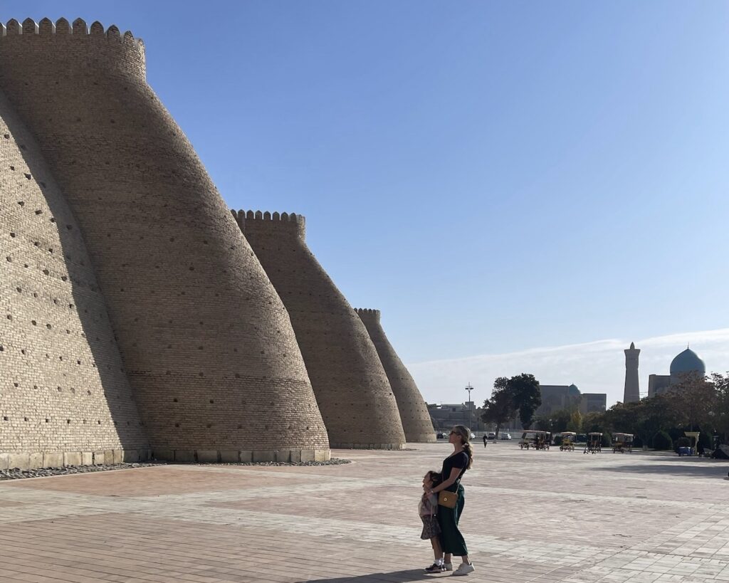 A photo of a woman and child looking up at the imposing stone walls of the Ark of Bukhara